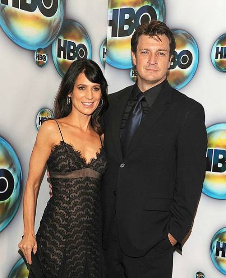 Nathan Fillion in a black suit poses a picture with Perrey Reeves.